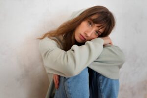 Chica joven mira esta sentada con las piernas abrazadas mirando con tristeza a la cámara